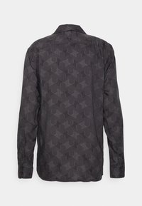Chemise noire à manches longues avec un motif géométrique gris rappelant un labyrinthe, vue de dos avec un col classique et des poignets boutonnés.