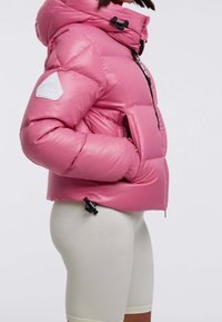 Rosa puffjacka med en glansig finish, oversized huva, dragkedja framtill, elastiska ärmslut, sidofickor och en logotyp på ärmen.