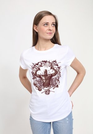 Ung kvinde med langt hår iført en hvid t-shirt med et detaljeret Deadpool-grafik, der holder to pistoler med krydsede sværd nedenunder.