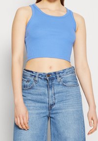 Top court en coton bleu à côtes associé à un jean en denim bleu clair taille haute, avec fermeture à boutons et design classique à cinq poches.