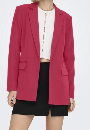 Kobieta w czerwonym żakiecie na białym krótkim topie z wycięciami, w połączeniu z czarną mini spódniczką z przednim rozcięciem.