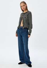 Cardigan à carreaux noir et blanc avec des boutons à l'avant, col rond et deux poches, associé à un jean en denim bleu ample.