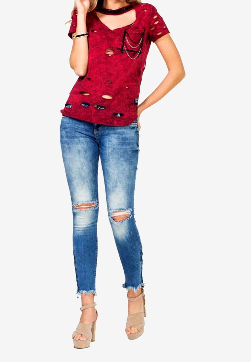 Röd sliten t-shirt med flera hål, ihop med blå skinny jeans med sprickor vid knäna, och beige högklackade sandaler.