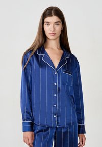 Navyblå satinpyjamas set med vita ränder, med en ficka, knäppning med knappar och kontrasterande mudd, som ger en slät textur.