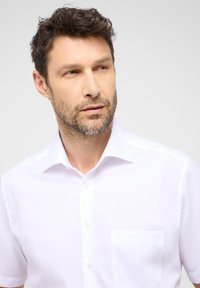 Kortekooien wit shirt gemaakt van stof met een gladde textuur, voorzien van een puntige kraag, knoopsluiting en een borstzak.