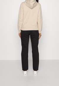 Felpa crema con cappuccio e tasca a marsupio, abbinata a jeans neri a gamba dritta e sneaker bianche. Vestibilità semplice e rilassata.