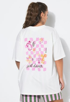 Femme aux longs cheveux foncés porte un T-shirt blanc oversize avec un motif à carreaux roses et des gribouillis sur le thème de la nourriture ainsi que les mots "girl dinner" au dos.
