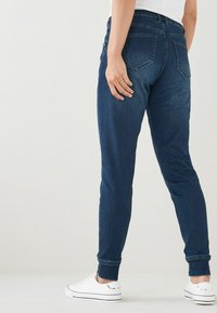 Tummansiniset farkut, slim fit -malliset, kapenevilla lahkeilla. Ominaisuuksiin kuuluvat takataskut ja ribbaus nilkkakäytävissä. Yhdistetty valkoisiin tennareihin.