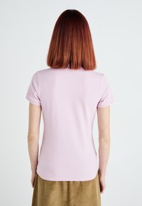Camisa polo de manga corta, de color rosa claro, con una textura suave y un dobladillo ligeramente curvado, combinada con una falda de pana marrón.