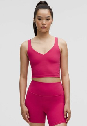 Prilagođeni, bez rukava, crop top i šortsevi visokog struka u vibrantnoj rozoj boji, glatke teksture, s V-izrezom i bez vidljivih logotipa.