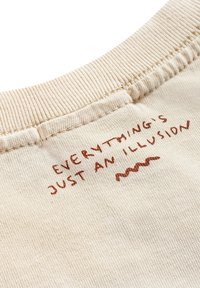 Materiał w kolorze kremowym o żebrowej teksturze; posiada czerwony haftowany napis "WSZYSTKO JEST TYLKO ILUZJĄ" z falistym wzorem poniżej.