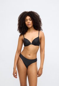 Μαύρο σουτιέν με επενδυμένα κύπελλα και ρυθμιζόμενους ιμάντες, συνδυασμένο με ταίριαστο κάτω μέρος μπικίνι με απαλό, μίνιμαλ σχέδιο και μέση μεσαίου ύψους.