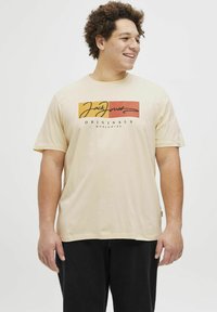 Beige tričko s krátkým rukávem vyrobené z bavlny, zdobené multibarevným grafickým designem s textem "Jack Jones Originals" v černé barvě.