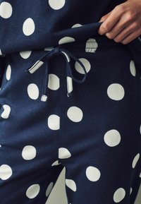 Pantaloni de lounge bleumarin cu buline albe, având talie elastică și șnur. Material moale cu o textură netedă.