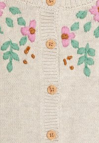 Cárdigan de punto en beige claro con bordados florales en tonos rosa pastel y verde. Presenta botones de madera y textura acanalada a lo largo de la abertura.