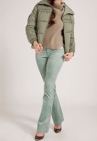 Veste matelassée vert clair avec des accents côtelés, pull en tricot beige et pantalon évasé en velours côtelé menthe, associés à des talons en imprimé léopard.