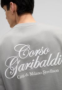 Grijze sweatshirt met geborduurde tekst "Corso Garibaldi Città di Milano Strellson" in het wit, met een ronde hals en een zachte textuur.