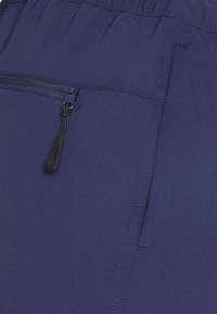 Tmavě modré sportovní šortky s elastickým pasem, zapínací kapsou a hladkou tkaninou s jemnými švy.