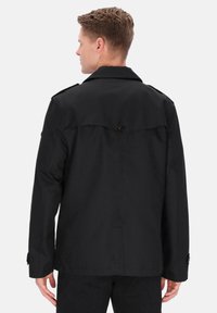 Sort jakke med knapdetalje bagpå, reverskrave og lange ærmer. Har en glat, tekstureret stof og skræddersyet pasform.