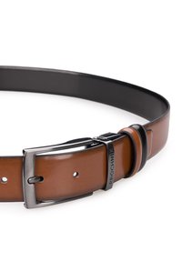 Brązowy skórzany pasek z czarną spodnią stroną, z metalową klamrą i znakiem firmowym. Gładka tekstura, z wieloma otworami do regulacji.