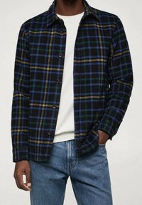 Geruit overhemd in donkerblauw, groen en gele tinten, met een knoopsluiting aan de voorkant, een spreidkraag en een zachte textuur, gedragen over een wit shirt.