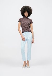 Bruin patroon top met korte mouwen en een hoge kraag, gecombineerd met lichtblauwe, op maat gemaakte broek en witte pumps met puntige neus.