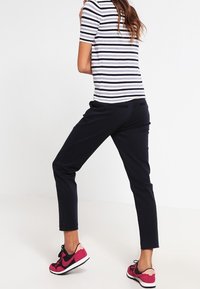 Top de manga corta a rayas en blanco y azul marino, pantalones negros y zapatillas Nike rosas. Los pantalones son ajustados y de longitud tobillo con una textura suave.