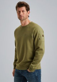 Sweatshirt vert olive avec col rond côtelé et manches raglan. Présente un logo discret sur la poitrine et des accents de boutons sur les manches.