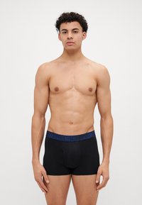 Schwarze Baumwollboxershorts mit einem blauen "Under Armour"-Logo am Bund, enganliegendes Design und ohne sichtbare Muster oder Akzente.