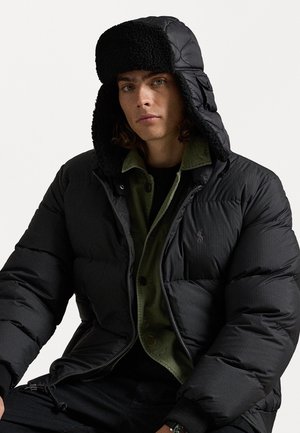 Čierna nafúknutá bunda s textúrovaným povrchom, s odnímateľnou kapucňou vystlanou kožušinou a pod ňou zelenou košeľou na gombíky.