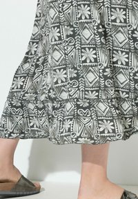 Jupe à motifs noir et blanc présentant des formes géométriques et des designs floraux, avec un ourlet froncé et une texture de tissu léger.