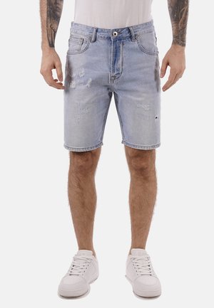 Pantalones cortos de mezclilla de color azul claro con un ajuste relajado, que presentan bordes deshilachados y detalles desgastados. Combinados con zapatillas blancas.