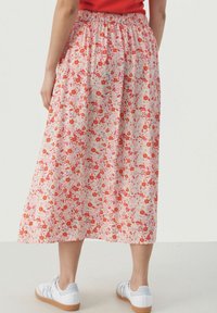 Jupe midi florale avec une base rose, ornée de fleurs rouges et oranges. Taille élastique et tissu doux, assortie à des baskets blanches.