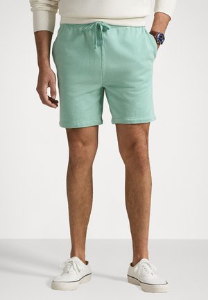 Shorts vert menthe en tissu doux, dotés d'une taille élastique avec cordon de serrage, de poches latérales et de ourlets retroussés. Portés avec des baskets blanches.