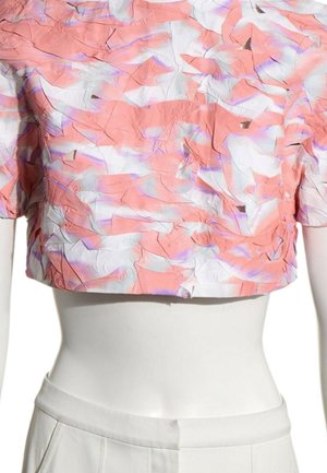 Kortærmet top med tekstureret, krøllet stof i rosa, hvid og lilla nuancer, båret på en hvid mannequin med hvide bukser.