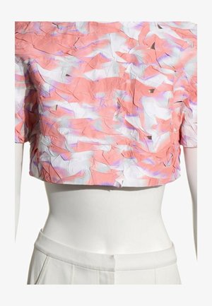Top corto de manga corta con tela texturizada y arrugada en tonos rosa, blanco y púrpura, usado en un maniquí blanco con pantalones blancos.