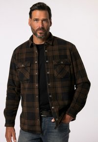 Camisa de franela a cuadros en negro y marrón con dos bolsillos en el pecho, botones a presión y una camiseta negra debajo, combinada con jeans azules.