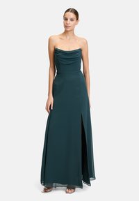 Dunkelgrünes, trägerloses Kleid mit drapiertem Oberteil, bodenlanger Optik, seitlicher Schlitze und glattem Satinmaterial. Silberelemente an der Fußbekleidung.