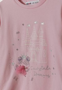 Ljusrosa T-shirt med ett slottstrykt med silverdetaljer och en karaktär som håller en stav, prydd med en tylle-fjäderdetalj.