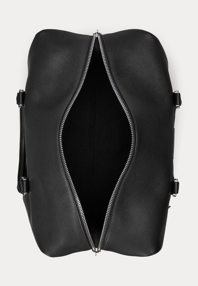 Sac de voyage en cuir noir avec fermeture éclair argentée partiellement ouverte, montrant un intérieur noir vide et des poignées latérales sur fond blanc.