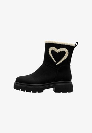 Bottines noires avec un tour de cheville en fausse fourrure texturée. Présentent un motif en forme de cœur crème sur le côté et une semelle épaisse pour plus de stabilité.