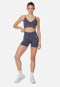 Sivý športový top a zodpovedajúce šortky s vysokým pásom vyrobené z elastického materiálu. Na šortkách je logo a top má tenké ramienka.