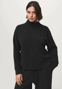 Sweatshirt en tricot noir avec un col montant, des manches raglan et une coupe décontractée. Texture douce et poignets côtelés, associé à un bas assorti.