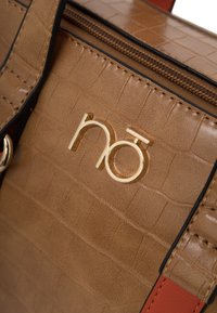 Sac à main synthétique marron texturé avec un logo doré, des accents rouges contrastants et un haut zippé. La surface présente un motif crocodile.