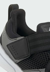 Chaussure de sport noire et grise dotée d'une tige en mesh respirant, d'une sangle texturée et d'une semelle blanche avec des détails perforés.