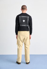 Svart langermet skjorte med mønstrete bakgrunn og logo, sammen med lysebeige cargo-bukser som har sidelommer og en avslappet passform.