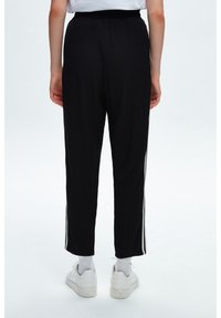 Svarta träningsbyxor med vita ränder på sidorna, med en avslappnad passform, elastisk midja och mjukt, lätt tyg. Bärs med vita sneakers.