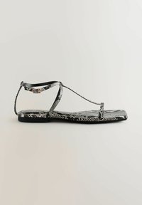 Černobílé ploché sandály s hadím vzorem, tenkými řemínky, nastavitelnou přezkou na kotníku a plochou podrážkou. Hladký povrch s minimalistickým designem.