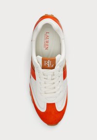 Balti ir oranžiniai sportbačiai, pagaminti iš suede ir odos medžiagų, su apvaliu pirštu, raištelių uždarymu ir tan spalvos logotipo pleistru ant liežuvio.