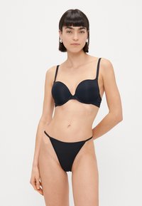 Sort polstret bh med justerbare stropper og sømløst design, parret med en matchende sort thong med minimal dækning og en glat tekstur.